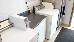 Un espace buanderie comprenant deux machines à laver blanches et un sèche-linge, un plan de travail et une porte dotée d’une poignée.