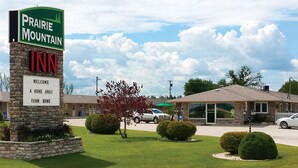 Une enseigne de l’hôtel Prairie Mountain, avec un message d’accueil, un pilier en pierre et une pelouse bien entretenue agrémentée d’arbustes.