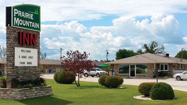 A Prairie Mountain Inn sign with a welcoming message, a stone pillar, and a well-maintained lawn with bushes.