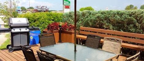Une terrasse extérieure avec une table et des chaises en verre, un barbecue et une poubelle.