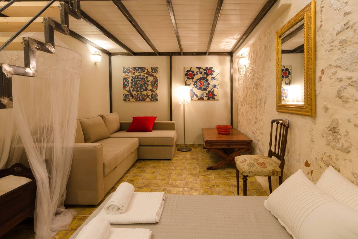 Ein Schlafzimmer mit Bett, einer Couch, einem Sessel, einem Tisch und Kunstwerken an den Wänden.
