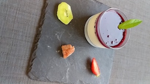 A dessert with a berry sauce, a slice of kiwi, a piece of orange candy, and a strawberry on a slate plate. - Hôtel Le Week-End (Plouider)