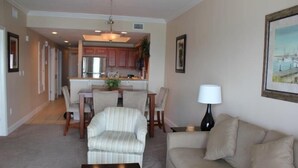 A living room with a sofa, a coffee table, a dining area with chairs and a table, and a kitchen in the background. - Seawind 1008 by ALBVR (Gulf Shores)