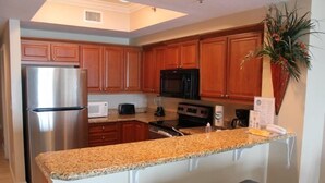 A kitchen with wooden cabinets, stainless steel appliances, granite countertops, and a small island with stools. - Seawind 1008 by ALBVR (Gulf Shores)