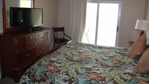 A bedroom with a bed, a television on a wooden dresser, a chair, and a lamp. - Seawind 1008 by ALBVR (Gulf Shores)