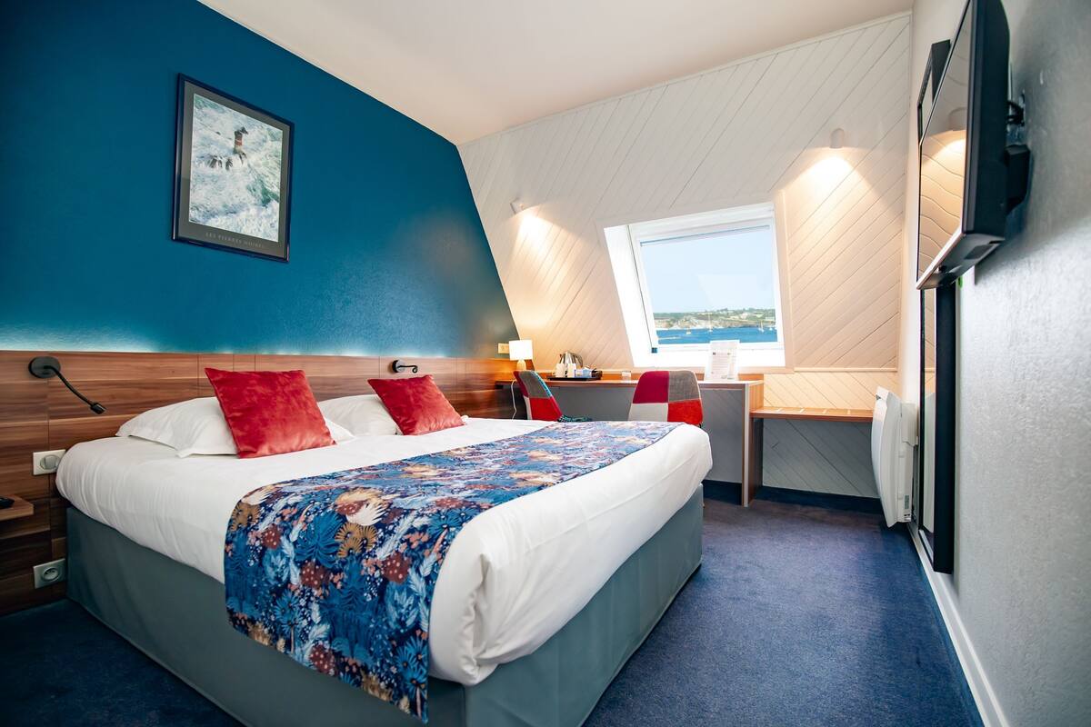 Une chambre d’hôtel moderne avec un grand lit, un bureau et une fenêtre donnant sur la mer.