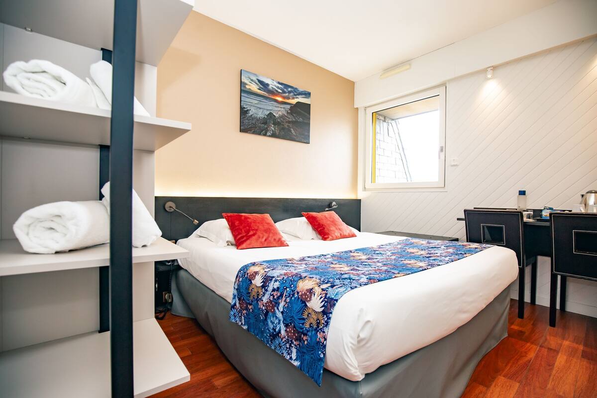 Une chambre d’hôtel moderne, équipée d’un lit, d’un bureau et d’une fenêtre.