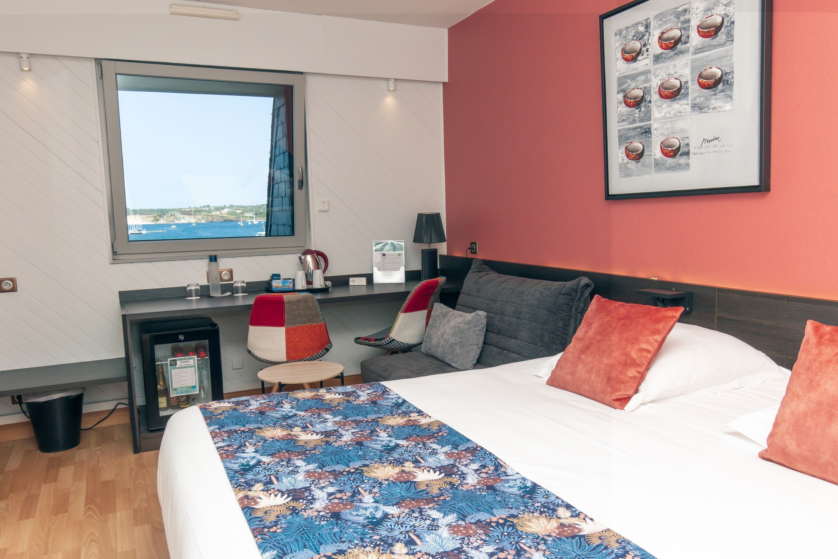 A hotel room with a large bed, a desk with a computer, a chair, a small table, a window with a view, and a framed picture on the wall.