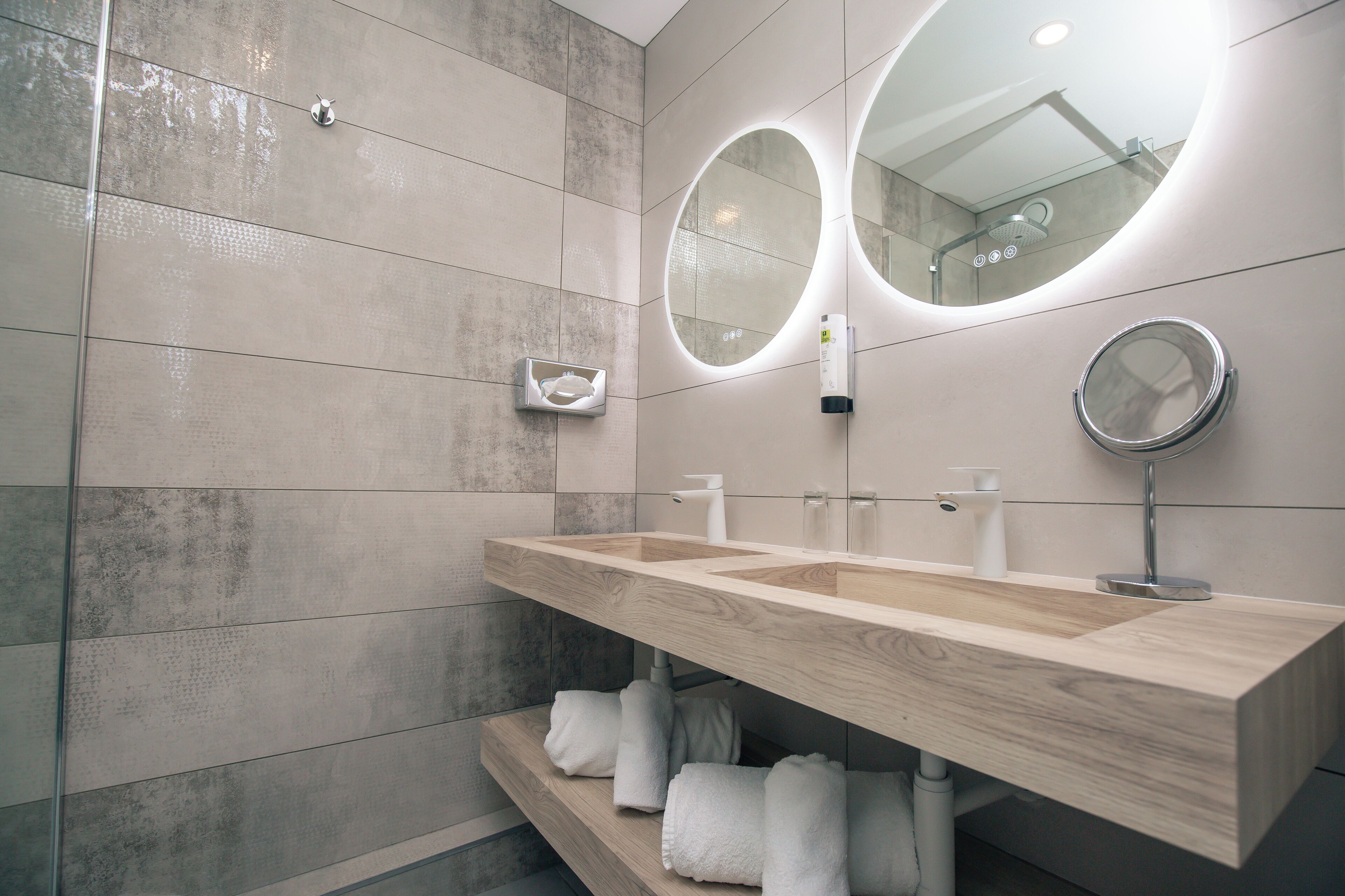 A modern bathroom with a wooden vanity, two mirrors, and a towel rack.
