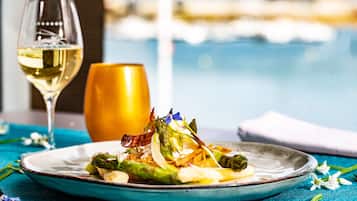 A plate of food with asparagus and other vegetables, a glass of white wine, and a golden vase on a table with a blue tablecloth.