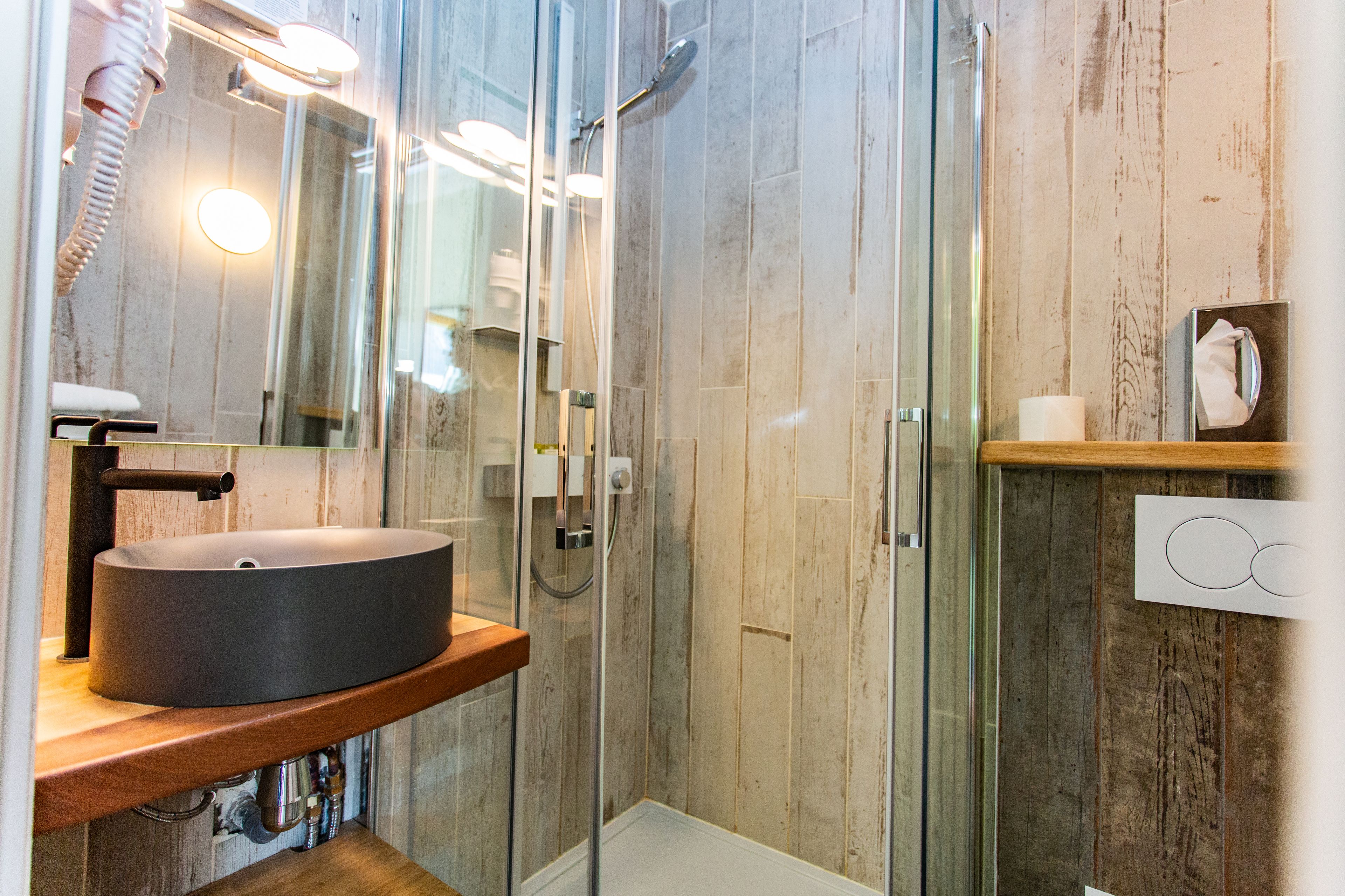 A modern bathroom with a glass-enclosed shower, a round sink, and a wooden vanity.