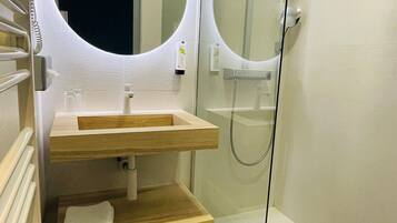 A modern bathroom with a glass-enclosed shower, a wooden vanity, and a round mirror.