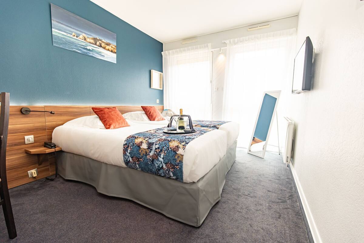 Une chambre d’hôtel avec un lit, un téléviseur à écran plat, un tableau au mur et une fenêtre avec des rideaux.