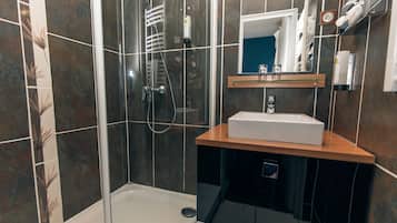 Un baño moderno con ducha de vidrio, un lavamanos blanco y un espejo encima.