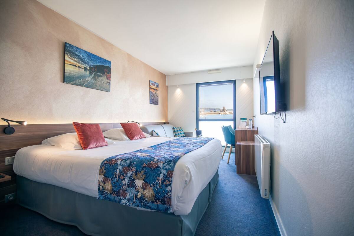 Une chambre d’hôtel avec un grand lit, un bureau avec une chaise, un téléviseur fixé au mur et une fenêtre donnant sur un beau paysage.