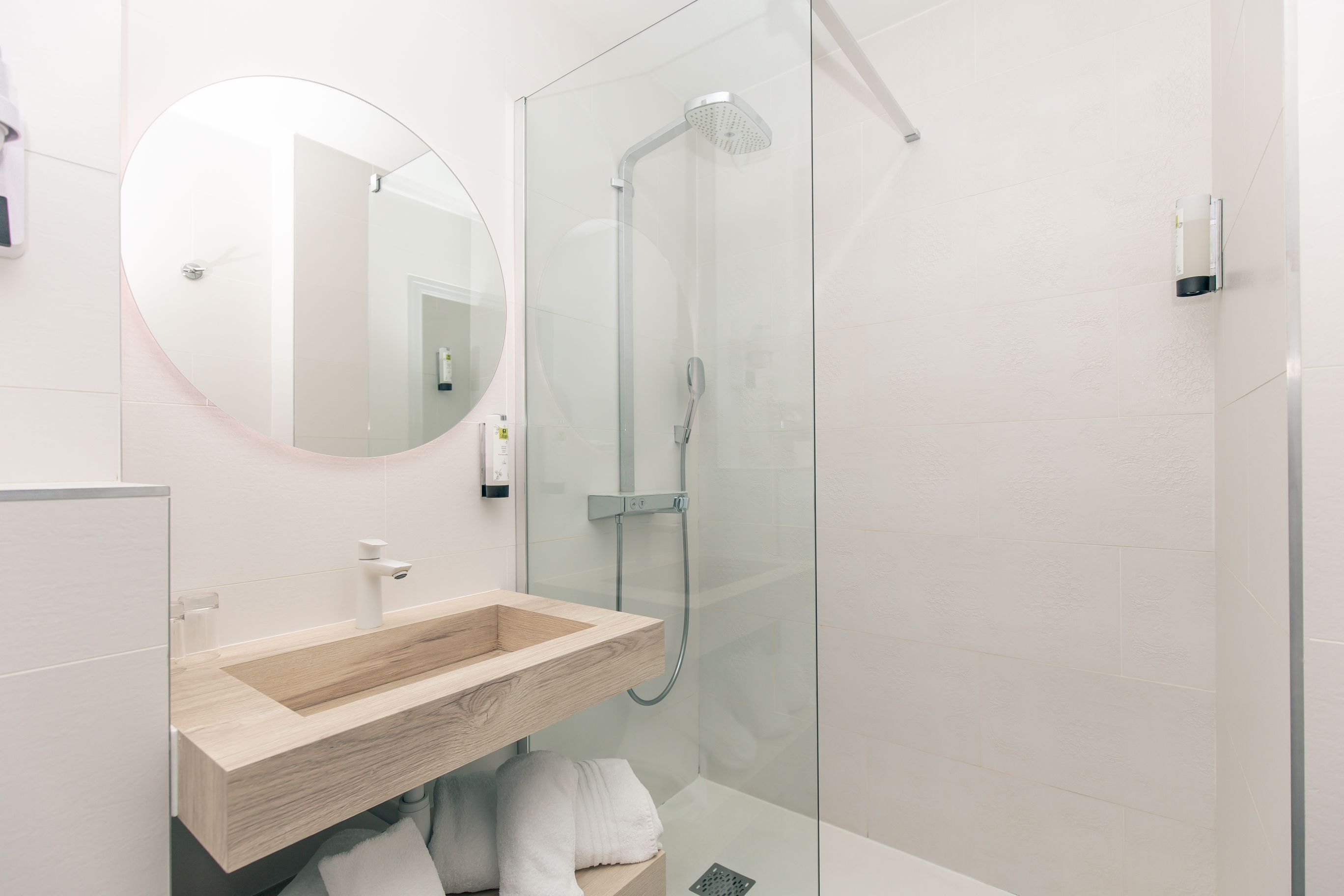 A modern bathroom with a wooden vanity, a round mirror, and a glass-enclosed shower.