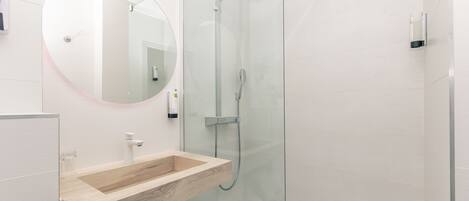 A modern bathroom with a wooden vanity, a round mirror, and a glass-enclosed shower.