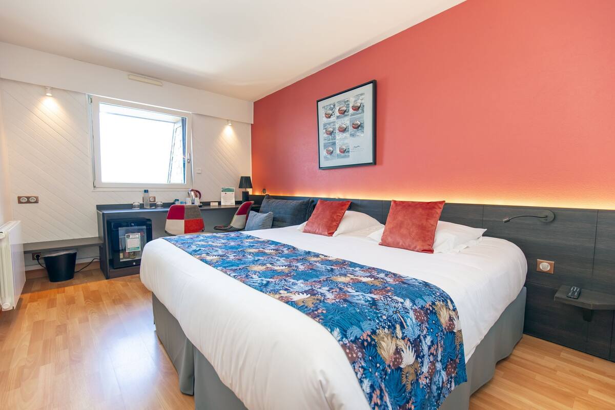 Une chambre d’hôtel moderne avec un grand lit, une table de chevet, un bureau et une fenêtre.