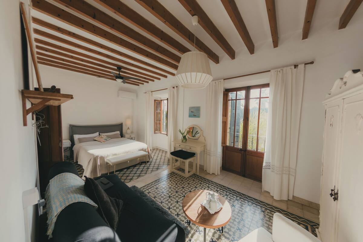 Une chambre à coucher avec un lit, un canapé, une petite table, un miroir et une fenêtre avec des rideaux.