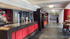 A modern bar area with a long counter, shelves with bottles, and a red accent wall. - The Lincoln Hotel (Lincoln)