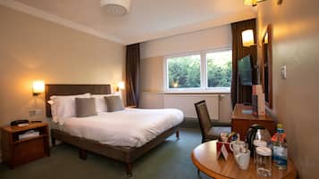 Ein Hotelzimmer mit einem Bett, Nachttischen, einem Schreibtisch mit Stuhl, einem Spiegel und einem Fenster mit Vorhängen.