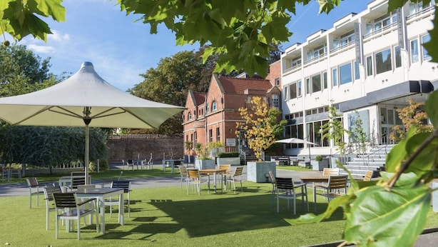 An outdoor seating area with tables and chairs, a large umbrella, and a building with a sign reading "GREEN ROOM BAR" in the background. - The Lincoln Hotel (Lincoln)