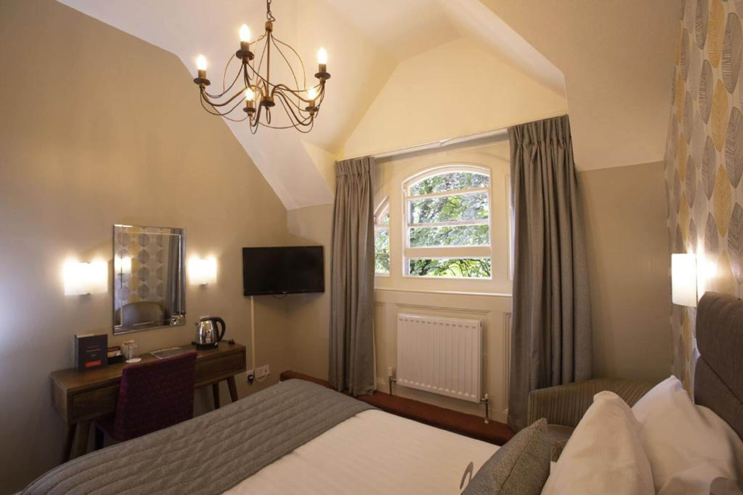 Una habitación de hotel con una cama grande, un escritorio con una silla, un televisor y una ventana con cortinas.