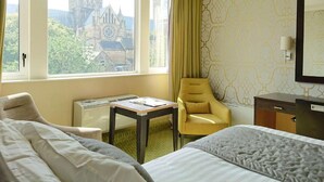 A hotel room with two beds, a desk, a chair, and a view of a church through large windows. - The Lincoln Hotel (Lincoln)
