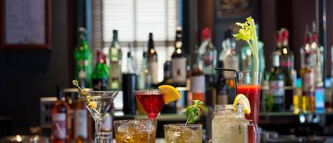 A bar with various drinks, including cocktails and a pitcher of iced tea, with bottles of alcohol in the background.