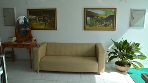 Una sala de estar con un sofá color beige, un escritorio de madera con un espejo, dos cuadros enmarcados y una planta en maceta.