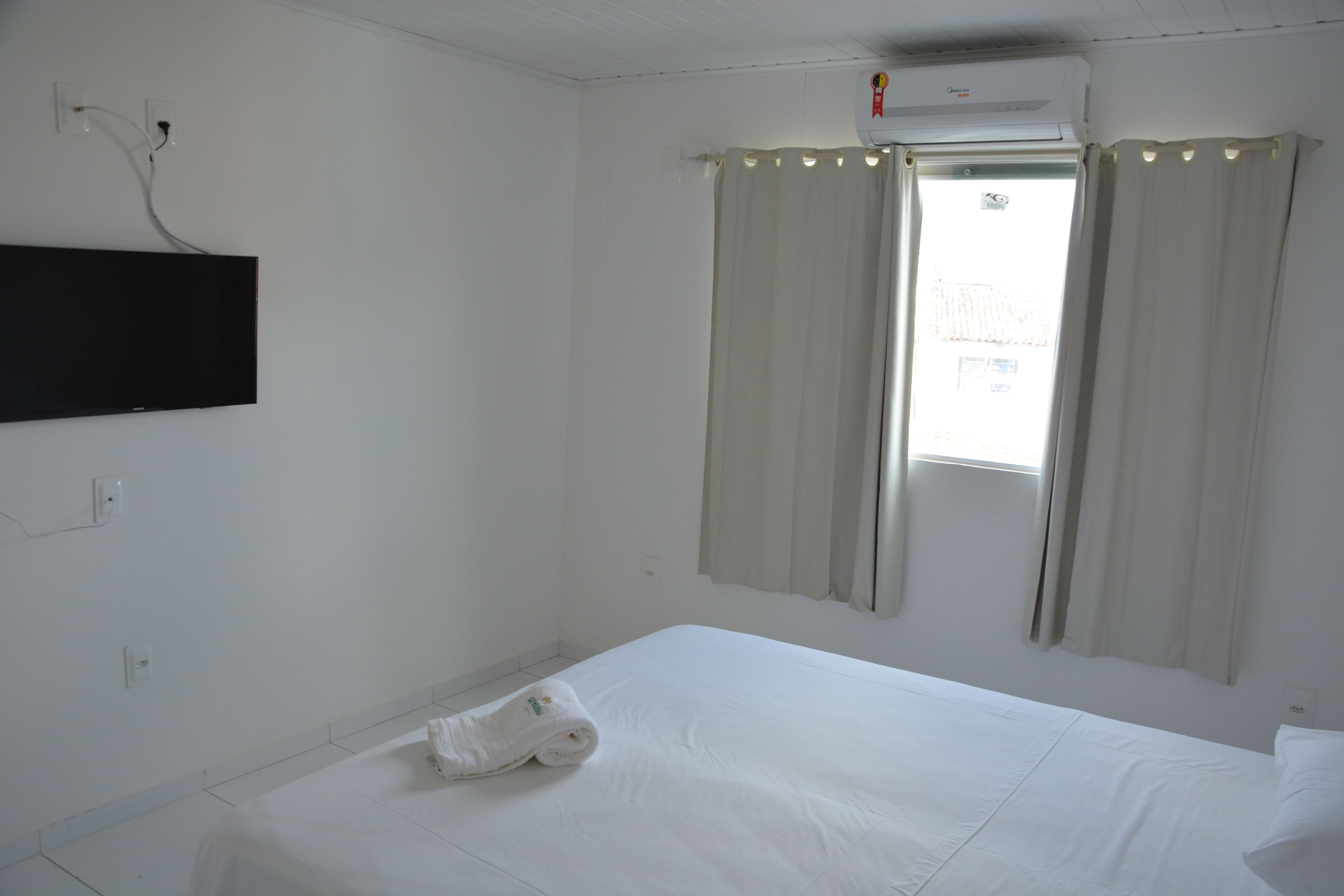 Una habitación de hotel con una cama, un televisor de pantalla plana en la pared y una ventana con cortinas.