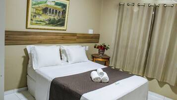 Ein Hotelzimmer mit einem Bett, einem Bild an der Wand, einer Vase mit Blumen und einem Vorhang.