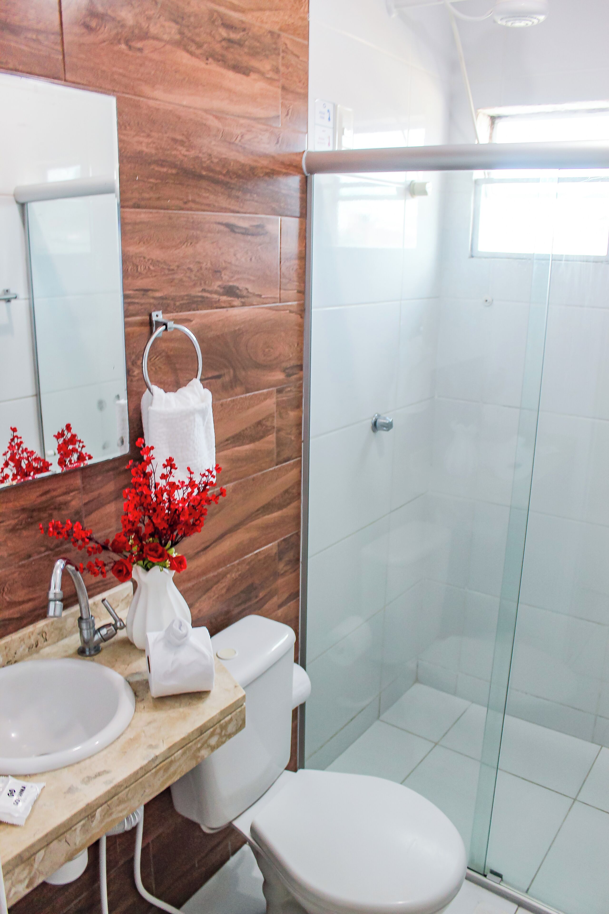 A bathroom with a wooden wall, a white sink, a toilet, a glass shower enclosure, and a mirror.