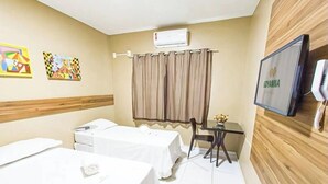 Habitación de hotel con dos camas, una mesita con un florero y un televisor en la pared, además de un equipo de aire acondicionado.