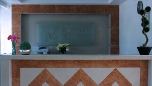 A reception desk with a glass display case, a potted plant, and a decorative tile pattern. - Hotel Zirahuen (Lazaro Cardenas)