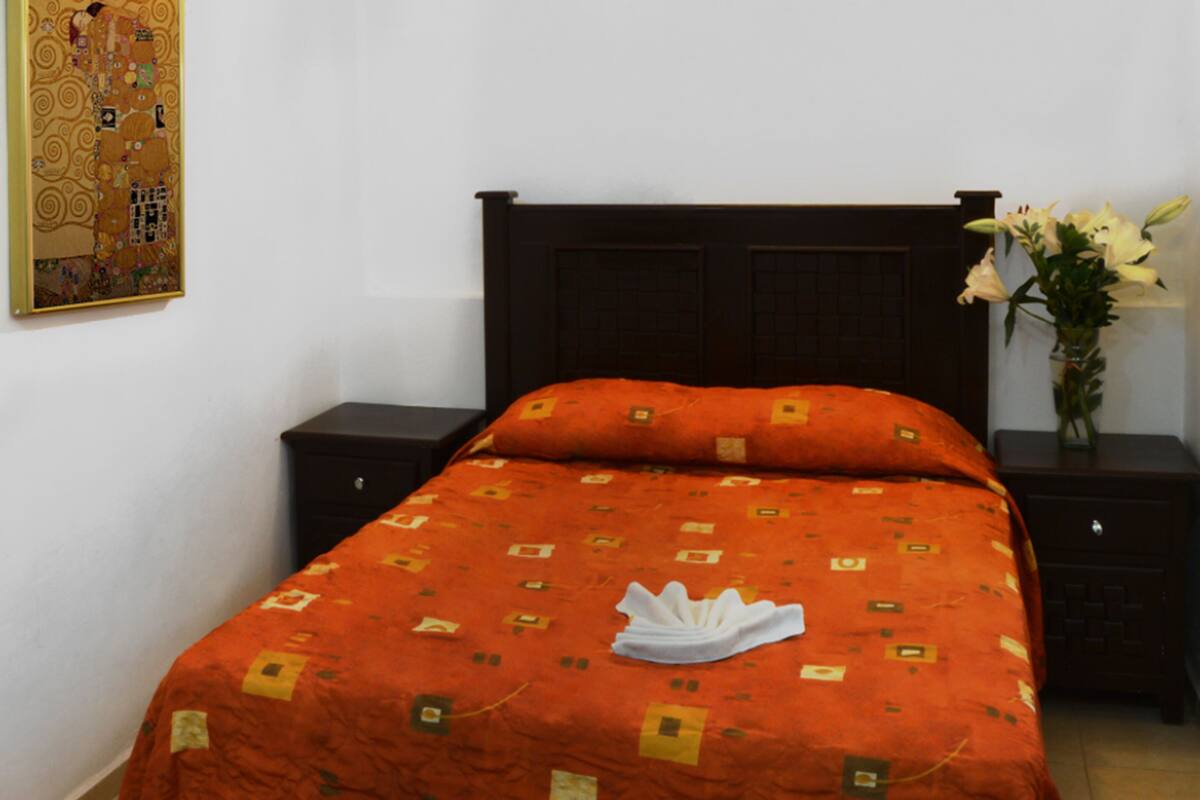 Een hotelkamer met een bed, een nachtkastje, een vaas met bloemen en een schilderij aan de muur.