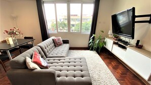 A living room with a grey sofa, a white rug, a TV, and a dining table with chairs. - Private Modern Apartment in Pardo - Miraflores (Lima)