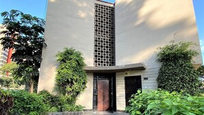 A building with a central vertical feature, a paved entrance, and surrounding greenery. - Private Modern Apartment in Pardo - Miraflores (Lima)