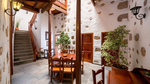 A rustic interior with a stone wall, wooden staircase, and a dining area with a table and chairs. - Hotel Rural Villa de Agüimes (Aguimes)