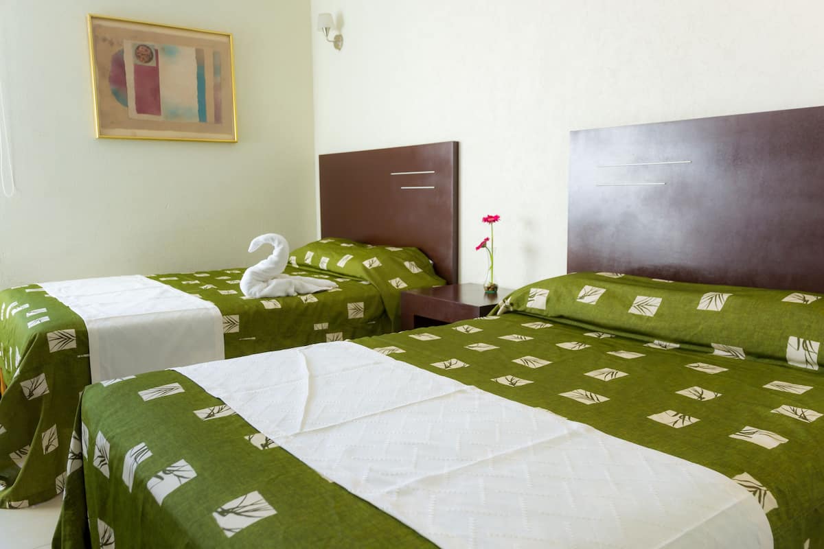 Habitación de hotel con dos camas individuales, cada una con ropa de cama verde y almohadas blancas. Hay un cuadro en la pared y un florero con una flor roja sobre la mesita de noche.