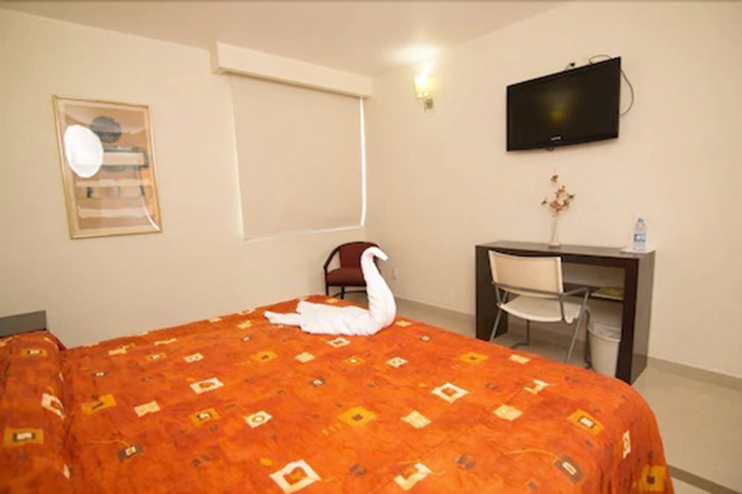 A hotel room with a bed, a desk, a chair, a television, and a window.