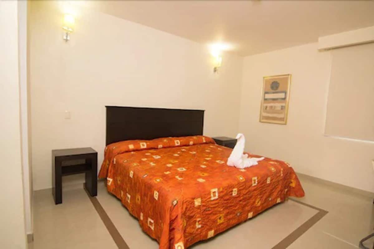 Habitación de hotel con una cama individual, una mesita de noche, una lámpara fijada en la pared y un certificado en un marco colgado.