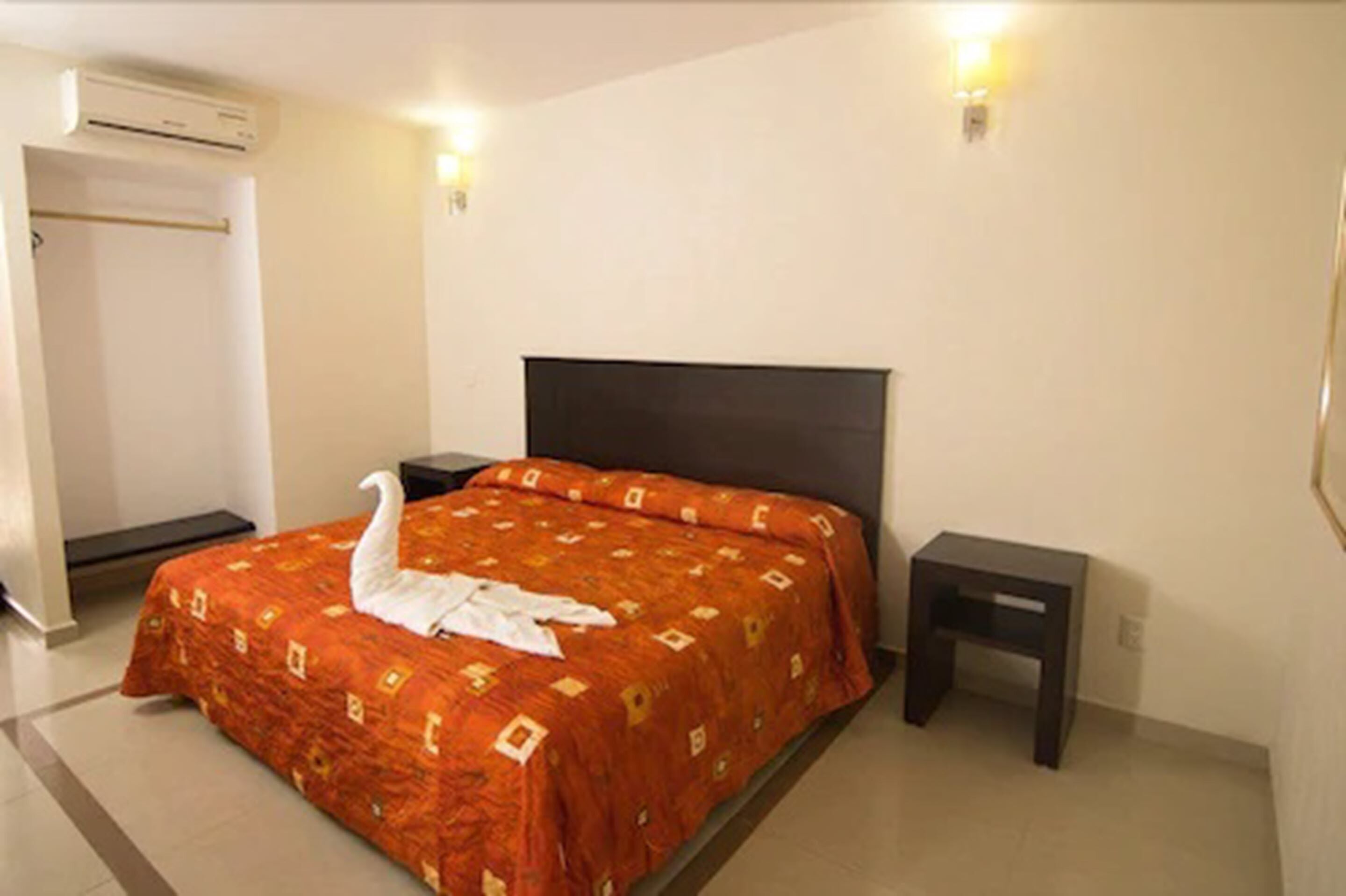 Quarto de hotel com cama, mesa de cabeceira, ar condicionado fixado na parede e luminária.