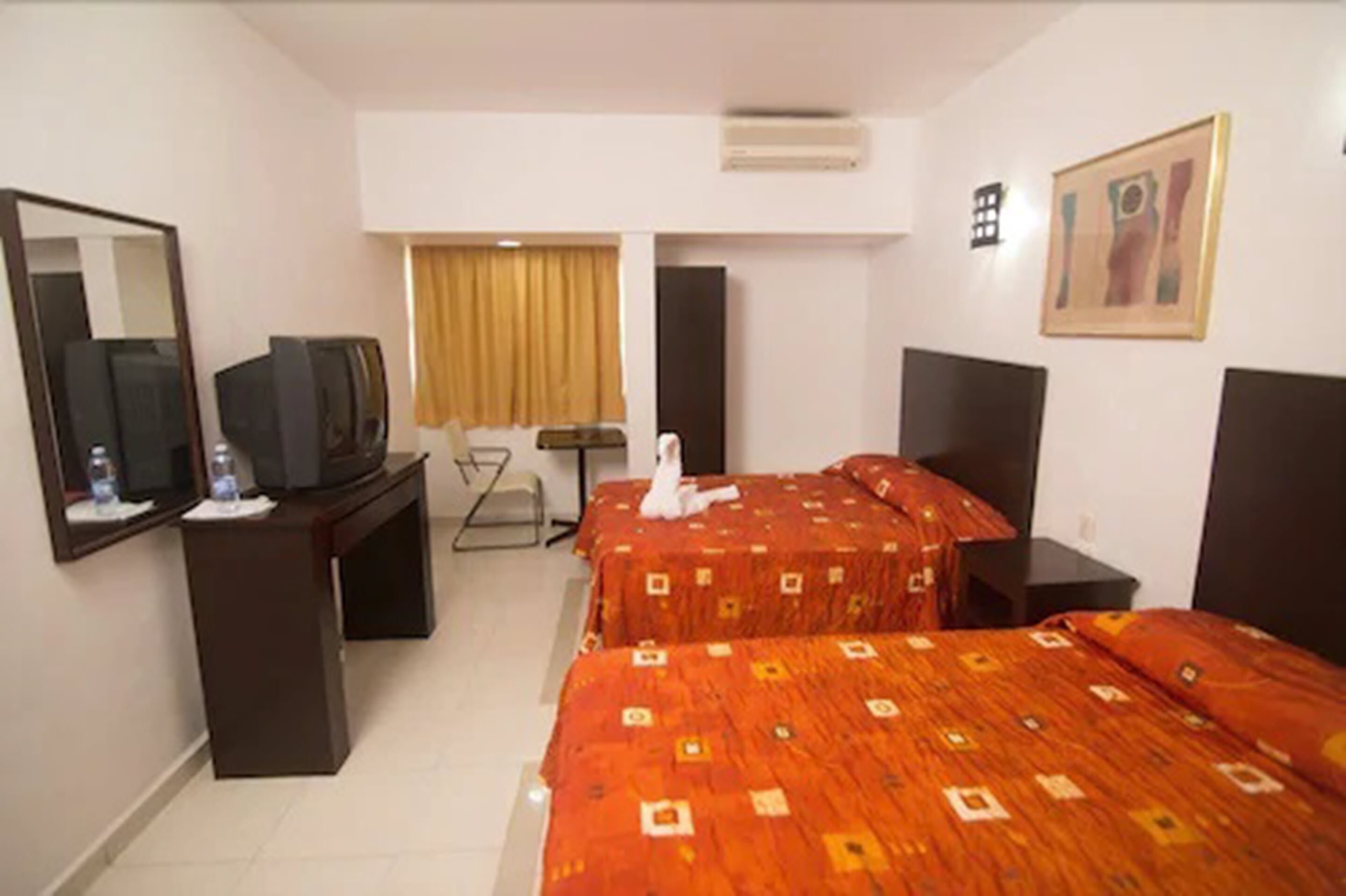 Een hotelkamer met twee bedden, een bureau met een televisie, een spiegel en een schilderij aan de muur.