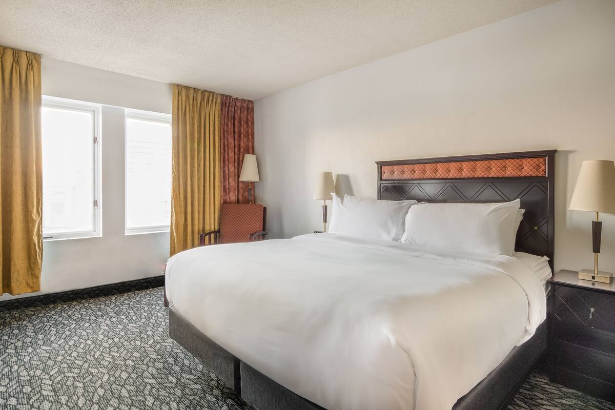 A hotel room with a large bed, two bedside lamps, a nightstand, and a window with curtains.