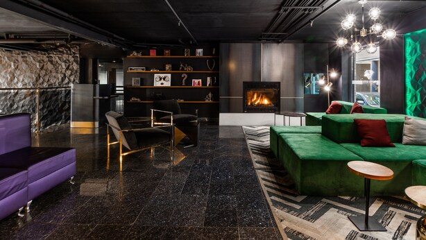 A modern interior with a fireplace, green and purple sofas, a bookshelf, and a patterned rug. - Lelux Hotel (Montreal)