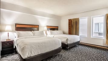 A hotel room with two beds, a nightstand with a lamp, a window with curtains, and a patterned carpet.