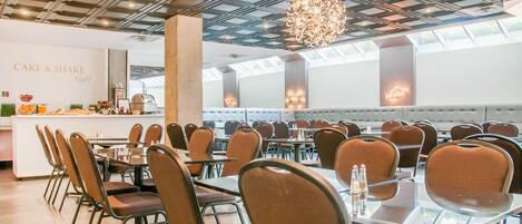 Un espace repas moderne avec un bar central portant l’inscription « CAKE & SHAKE », entouré de tables et de chaises.