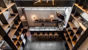 A modern bar area with a central bar counter, stools, and shelves on either side. - Lelux Hotel (Montreal)