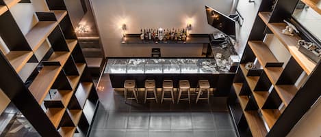 Zona de bar moderna con barra central, taburetes y estanterías a ambos lados.